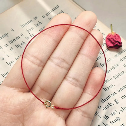 Red string bracelet on a hand with a book and dried flower in the background