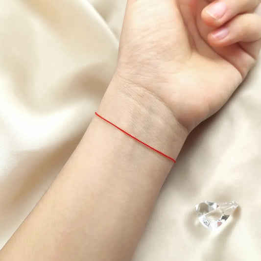 Close-up of a wrist wearing a red string bracelet on a soft beige background