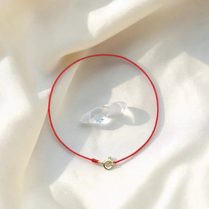 Red string bracelet with a clear crystal on a light fabric background