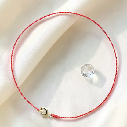 Red string bracelet with a gold clasp on a white surface