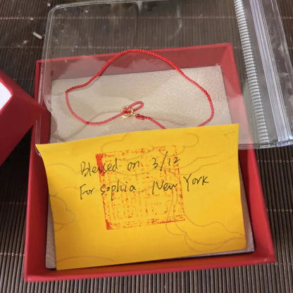 Small red box with a yellow card inside, containing a red string and small object on a textured surface.