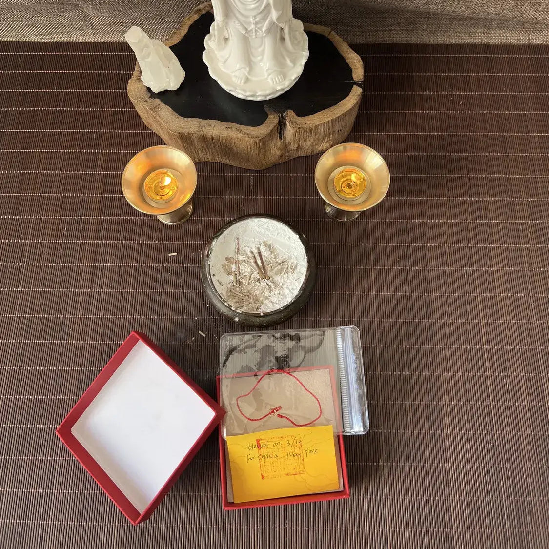 White statue on a wooden base with two candles and a small box on a textured surface.